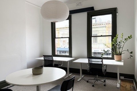 View from studio door, looking out to 2 height adjustable desks, 2 ergonomic chairs and round meeting table with chairs